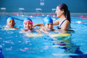 A group of children are having a swimming lesson in a pool. An adult is teaching them.