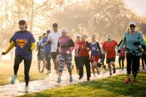 A group of people run through a park, it is raining