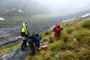 Three men are standing in a mountain range setting a trap
