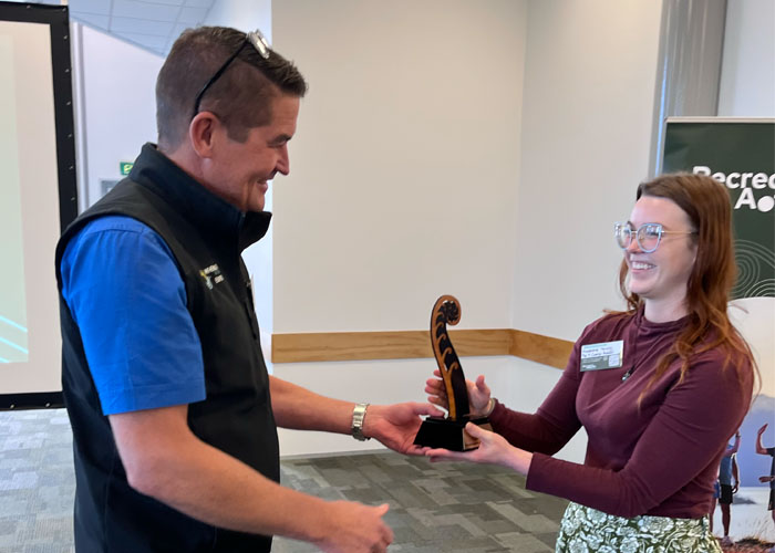 Man hands a smiling woman a wooden fern shaped award.