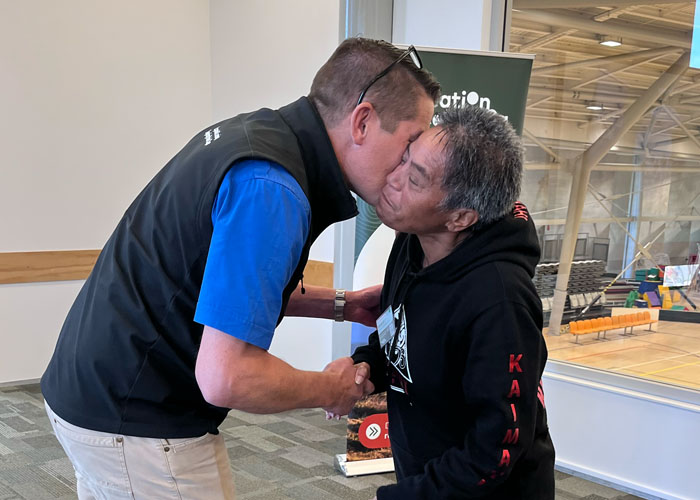 Man on a stage hands a woman a large award which is a Māori carving