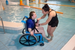 A woman is supporting a man in a wheelchair in a pool