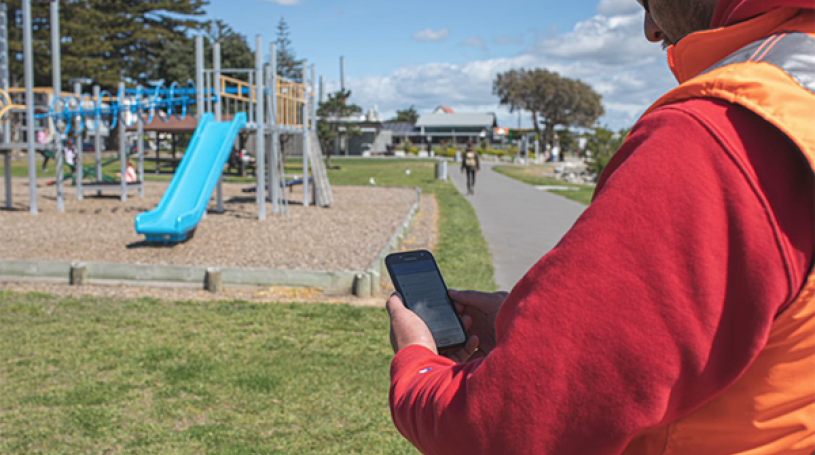 Man standing at a playground making notes into a tablet