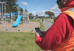 Man standing at a playground making notes into a tablet
