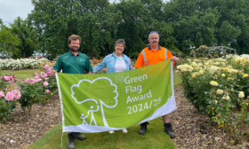 Three people standing holding a Green Flag Award flag