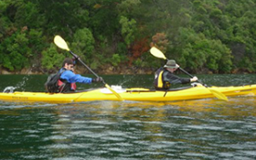 Two people kayak down a river in a double canoe