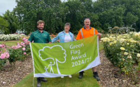 Three people standing holding a Green Flag Award flag