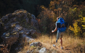 A man walks along a rocky hilltop. He has walking poles. He has a prosthetic leg